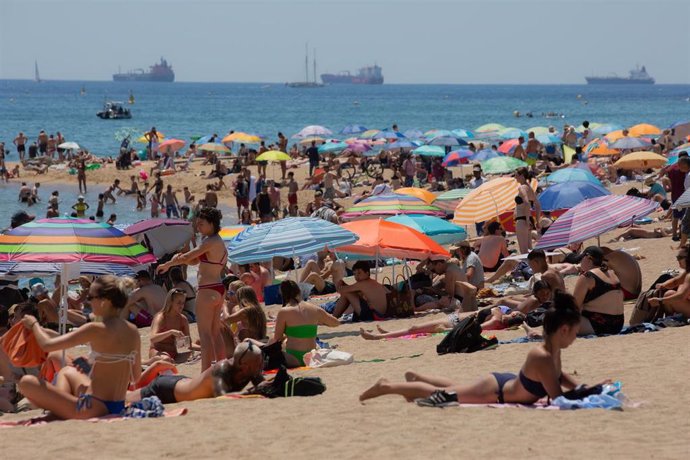 Varias personas se protegen del sol en la playa de la Barceloneta, a 13 de julio de 2022, en Barcelona, Catalunya (España). La intensa y extensa ola de calor llega hoy a su momento cumbre, aunque ese pico se mantendrá durante varios días seguidos, según