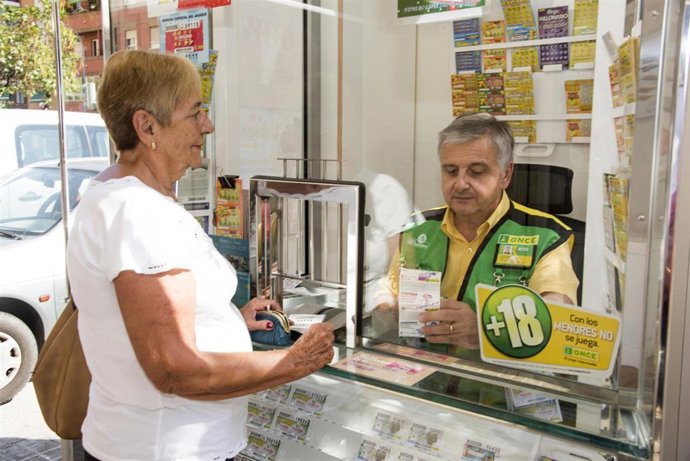 Tr. Valencia (C. A. Valenciana). 17/10/18.-Agente Vendedor Once, Con El Nuevo Chaleco Que Tienen Que Llevar (Uniforme) Para Ejercer La Venta - Venta Con Tpvlugar: Valenciaimagen: Vendedor De Cupón Con Clienta, Ejerciendo La Venta En Kiosco - Con Chaleco