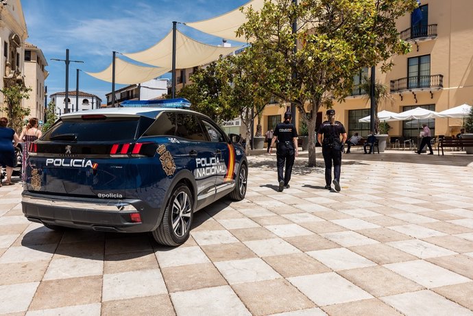 Archivo - Imagen de archivo de un coche de la Policía Nacional y dos agentes patrullan en una calle