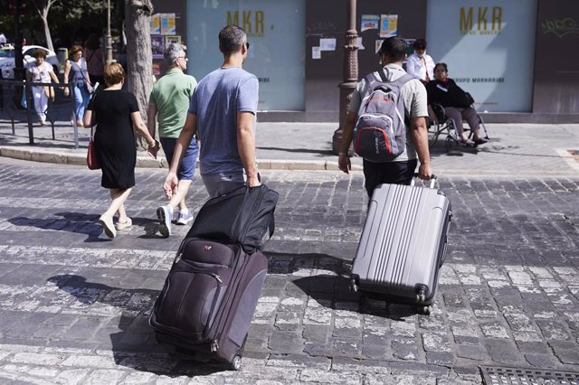 Archivo - Dos turistas, con maletas, cruzan un paso de peatones.