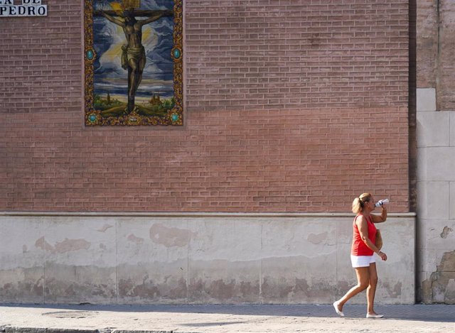 Una mujer bebiendo por la fachada de la Iglesia de San Pedro en otro día con altas temperaturas en la capital andaluza a 25 de julio del 2022 en Sevilla (Andalucía, España)