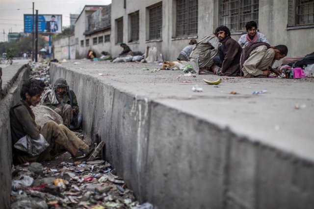 Archivo - Un hombre afgano se sienta en una zanja llena de basura mientras otros consumen drogas al lado de una carretera en Kabul.