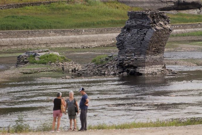 Tres personas junto al río Miño, cuyo bajo caudal ha dejado a la vista las ruinas del antiguo Portomarín, que en los años 60 del siglo pasado fue anegado por el embalse de Belesar, en Escairón, a 9 de agosto de 2022, en Escairón, Lugo, Galicia (España).