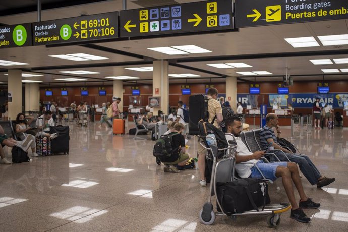 Varias personas esperan sentadas con sus maletas en el Aeropuerto Josep Tarradellas Barcelona-El Prat, a 8 de agosto de 2022, en Barcelona, Catalunya (España).  