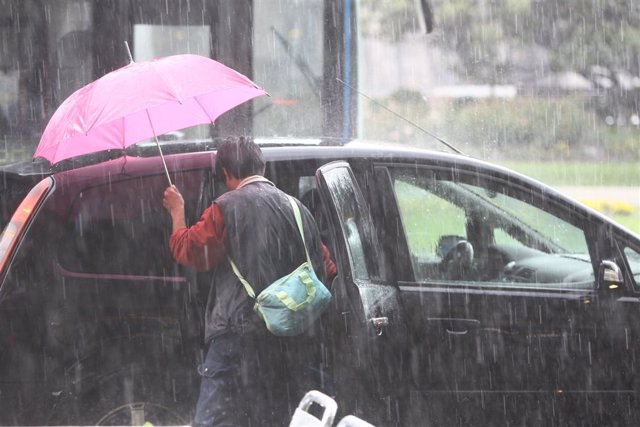 Archivo - Un hombre sujetando un paraguas entrando en su vehículo en medio de una tormenta.