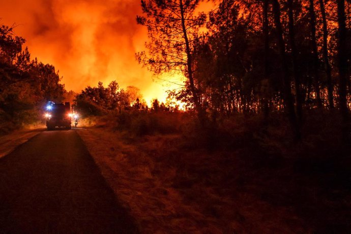 FILED - 11 August 2022, France, Belin-Beliet: A fire truck drives on a road past the flames of a forest fire near Belin-Beliet. French officials have warned that the forest fire could spread further in the southwest of the country. Photo: Thibaud Moritz