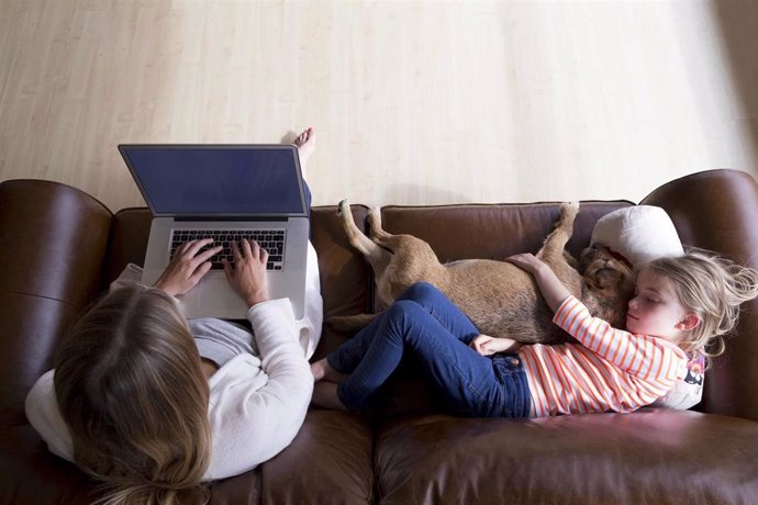 Archivo - Ariel view of a woman using a laptop whilst her daughter is sleeping next to her, cuddling their pet dog.