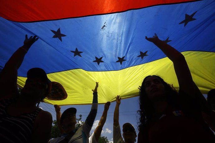 Archivo - 06 April 2019, Venezuela, San Diego: People walk under a national flag during a rally to in support of Venezuela's self-proclaimed interim president Juan Guaido against the government of incumbent President Nicolas Maduro. Photo: Juan Carlos H