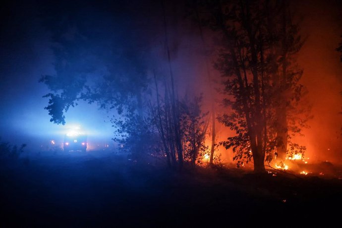 11 August 2022, France, Belin-Beliet: A fire truck drives on a road past the flames of a forest fire near Belin-Beliet. French officials have warned that the forest fire could spread further in the southwest of the country. Photo: Thibaud Moritz/AFP/dpa