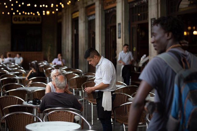 Archivo - Un camarero de origen extranjero atiende la terraza de un bar en Barcelona