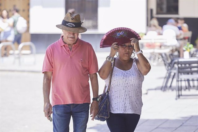 Archivo - Una señora se protege con el abanico del sol mientras el hombre lo hace con un sombrero en el centro de Sevilla