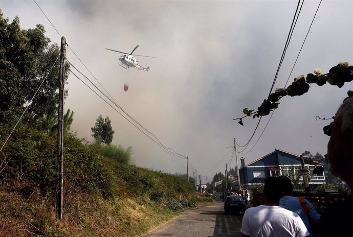 Un helicóptero entre el humo, trabaja con una cuba de agua en el incendio, a 22 de agosto, en la parroquia de Meira, en Moaña, Pontevedra, Galicia (España). El fuego declarado en una zona de eucaliptos, ha obligado a cortar la autovía de O Morrazo entre