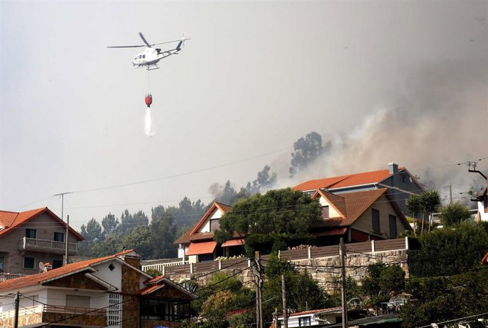 Un helicóptero trabaja con una cuba de agua en el incendio, a 22 de agosto, en la parroquia de Meira, en Moaña, Pontevedra,