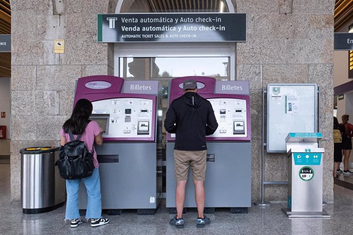 Dos personas compran billetes en los cajeros de venta automática en una estación de trenes