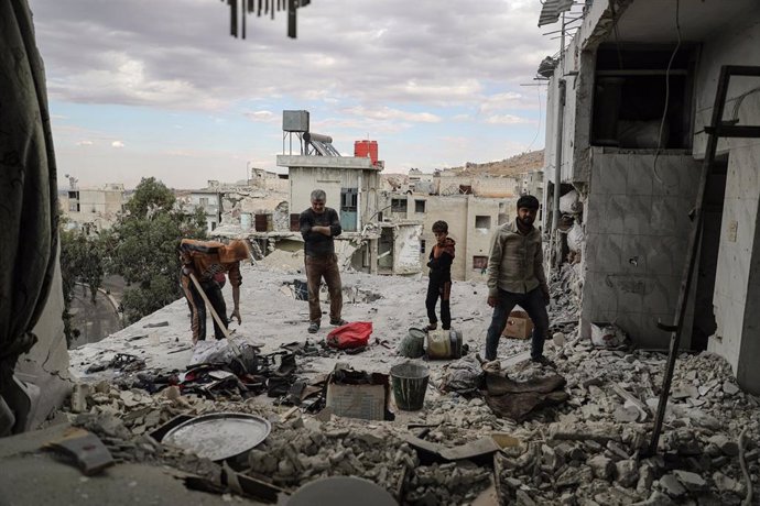 Archivo - Un grupo de personas pasea por los escombros de su casa en Ariha, oeste de Siria, tras un bombardeo (archivo). 