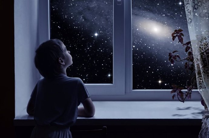 Niño mirando las estrellas por la ventana.