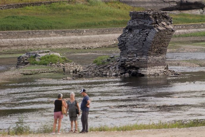 Tres personas junto al río Miño, cuyo bajo caudal ha dejado a la vista las ruinas del antiguo Portomarín, que en los años 60 del siglo pasado fue anegado por el embalse de Belesar, en Escairón, a 9 de agosto de 2022, en Escairón, Lugo, Galicia (España).