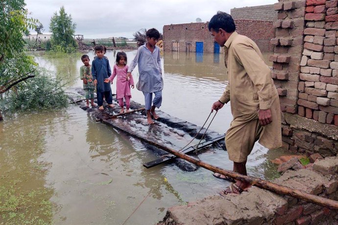 Un hombre ayuda a un grupo de niños a cruzar a un lugar seguro en un puente improvisado en medio de las inundaciones causadas por los fuertes aguaceros