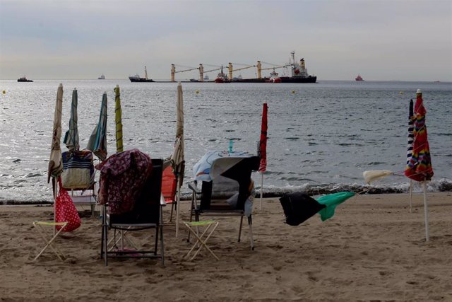 Personas en la playa observan como las actividades sobre el buque granelero OS35.