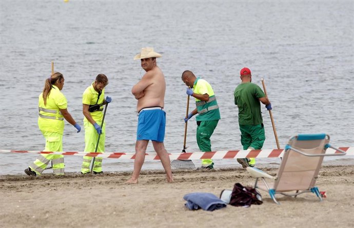 Un bañista en la playa de Poniente de La Línea mienrtas los operarios retiran restos del vertido del OS35.