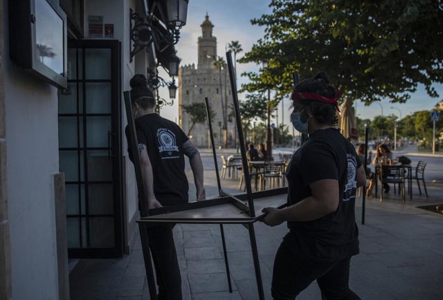 Archivo - Varios camareros recogen el mobiliario de la terraza de un bar, en una foto de archivo.