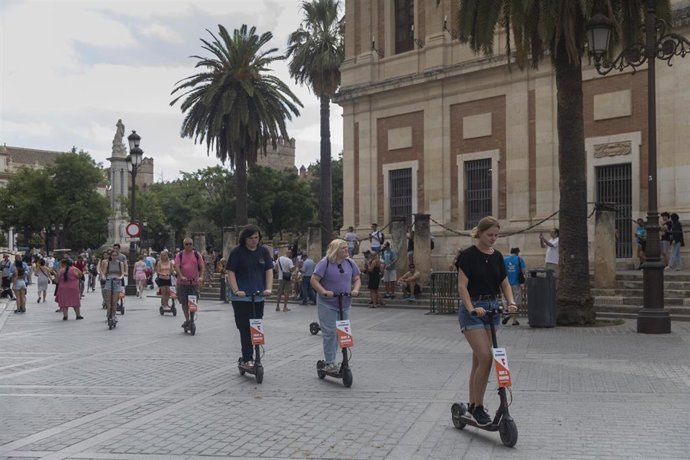 Turistas en patinete eléctrico paseando por el entorno de la Catedral. A 11 de agosto de 2022, en Sevilla (Andalucía, España).