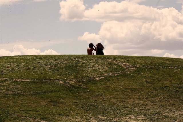 Archivo - Una pareja de jóvenes disfruta de un soleado día sentados en el césped del parque de las 'Siete Tetas' de Vallecas.