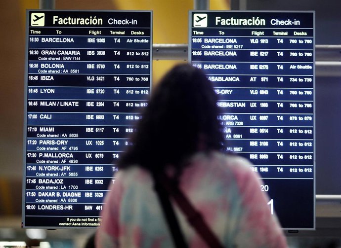 Archivo - Una mujer observa la pantalla informativa de vuelos en un aeropuerto. 