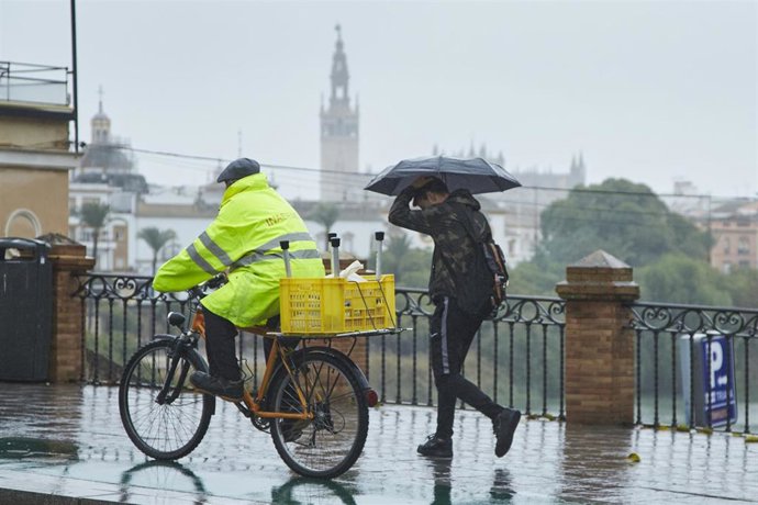 Archivo - Un ciclista y un joven, cruzando el Puente de Isabel II en un día lluvioso 