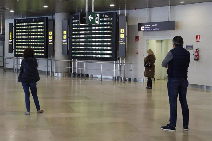 Archivo - Varias personas miran las pantallas luminosas en las que se muestra la información de los vuelos en el Aeropuerto de Valencia