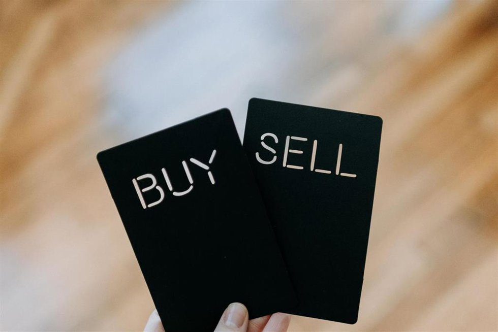 Una persona sostiene dos tarjetas de 'Compra' y 'Venta'. 