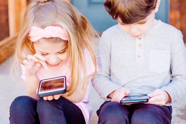Una niña y un niño usando un teléfono móvil