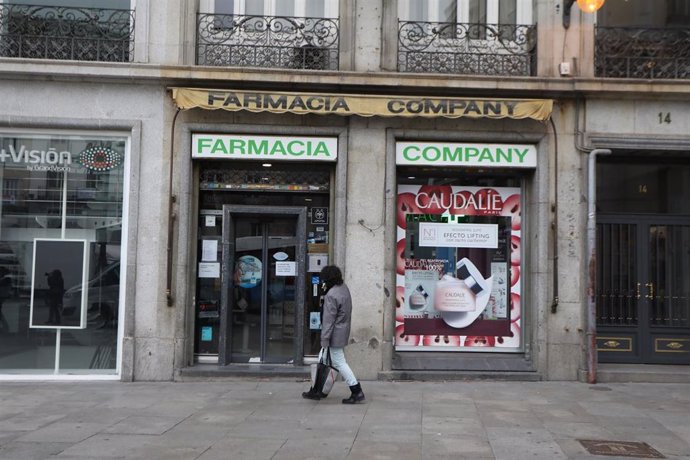 Archivo - Una mujer protegida con mascarilla y guantes pasa delante de una Farmacia un día después de que el ministro del Interior, Fernando Grande-Marlaska, anunciara que a finales de esta semana no habrá "ningún problema de abastecimiento" de mascaril