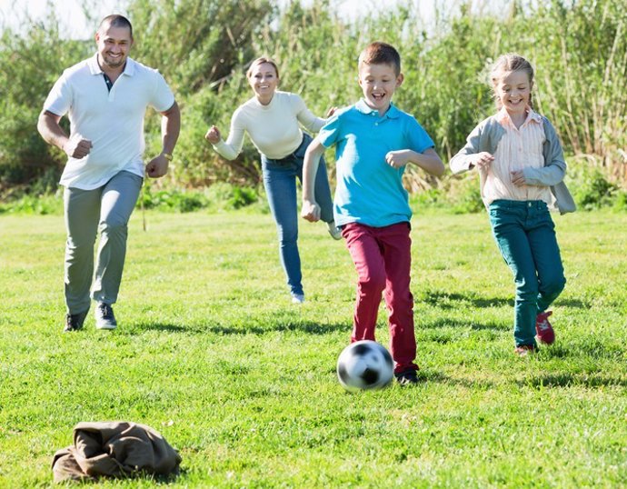 Archivo - Mother and father with two kids  running after  ball