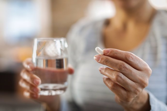 Archivo - Female hands hold pill and glass of water