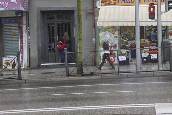 Una chica camina con un paraguas por la acera,