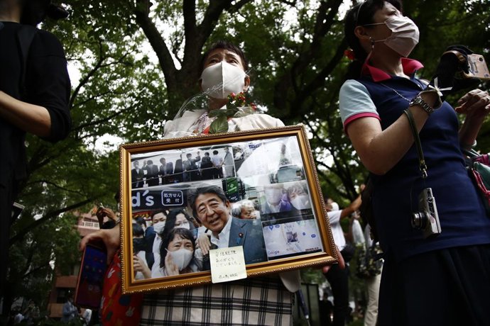 Archivo - 12 July 2022, Japan, Tokyo: A woman holds her memorial pictures with former Prime Minister Shinzo Abe while the hearse carrying his body leaves the Zojoji temple in Tokyo. A 41-year-old Japanese man on 8 July 2022 shot Abe from behind with a h