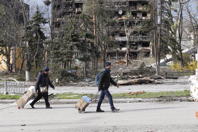 Archivo - Dos personas caminan frente a un edificio dañado por la guerra en la ciudad de Mariúpol, en el sureste de Ucrania