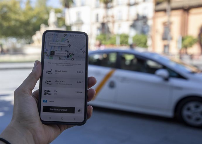 Imagen de un usuario con su teléfono móvil consultando los VTC ante una parada de taxis.