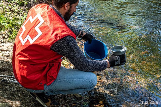 Voluntario de Cruz Roja recoge una muestra de agua en un río para analizar la presencia de microplásticos y otras sustancias contaminantes.