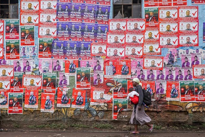 Una mujer carga con su hijo mientras pasea por delante de carteles electorales.