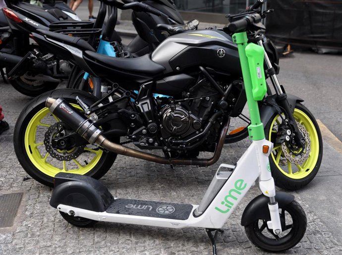 Un patinete eléctrico aparcado en la calle junto a motos.