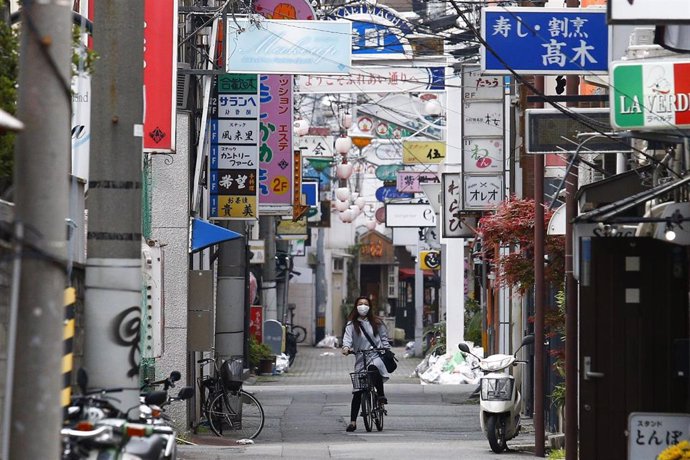 Archivo - Una mujer con mascarilla recorre en bicicleta una calle de Tokio