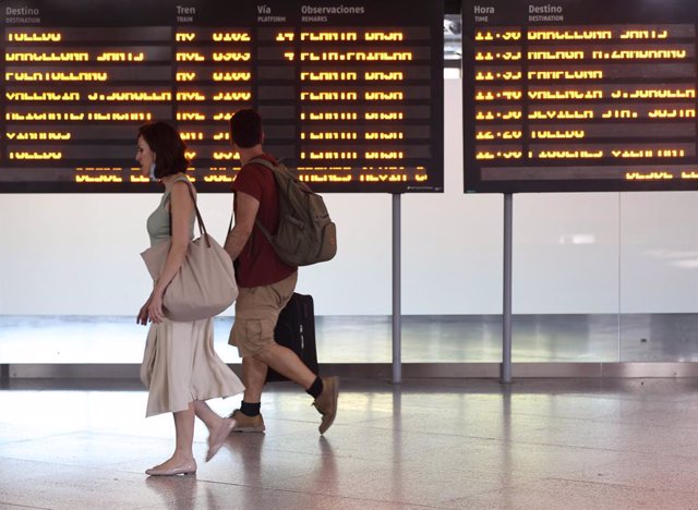 Archivo - Dos personas pasan por delante del panel de salidas de trenes en la estación de Atocha, a 29 de julio de 2022, en Madrid (España).  