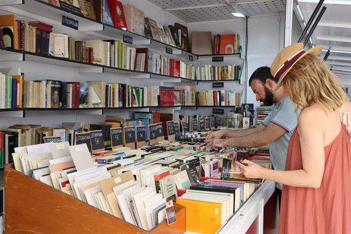 Archivo - Un par de personas visitan un stand de una Feria del Libro. 