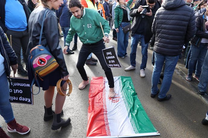 15 October 2022, Belgium, Brussels: Aprotester steps on the Iranian flag during a protest against the political regime in Iran. Photo: Nicolas Maeterlinck/BELGA/dpa