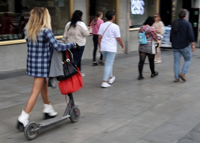 Una mujer camina con un patinete eléctrico,