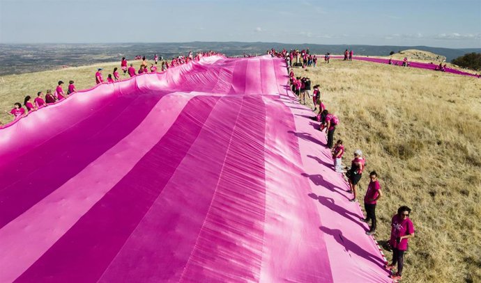 Voluntarios colocan un lazo rosa confeccionado con 5.720 metros cuadrados de tela en la cima de Las Tetas de Viana, a 8 de octubre de 2022, en Trillo, Guadalajara, Castilla-La Mancha (España). Más de 500 voluntarios han logrado el prestigioso Récord Gui