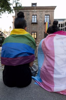 Archivo - Dos personas se arropan con la bandera LGTBI durante una sentada contra el "boicot" al Orgullo en la Plaza del Rey