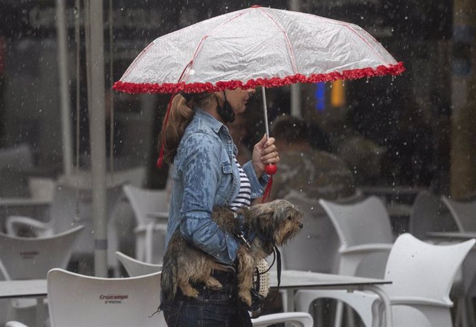 Archivo - Una mujer lleva a su perro en brazos bajo una tormenta. A 14 de septiembre de 2021, en Sevilla (Andalucía, España). (Foto de archivo).